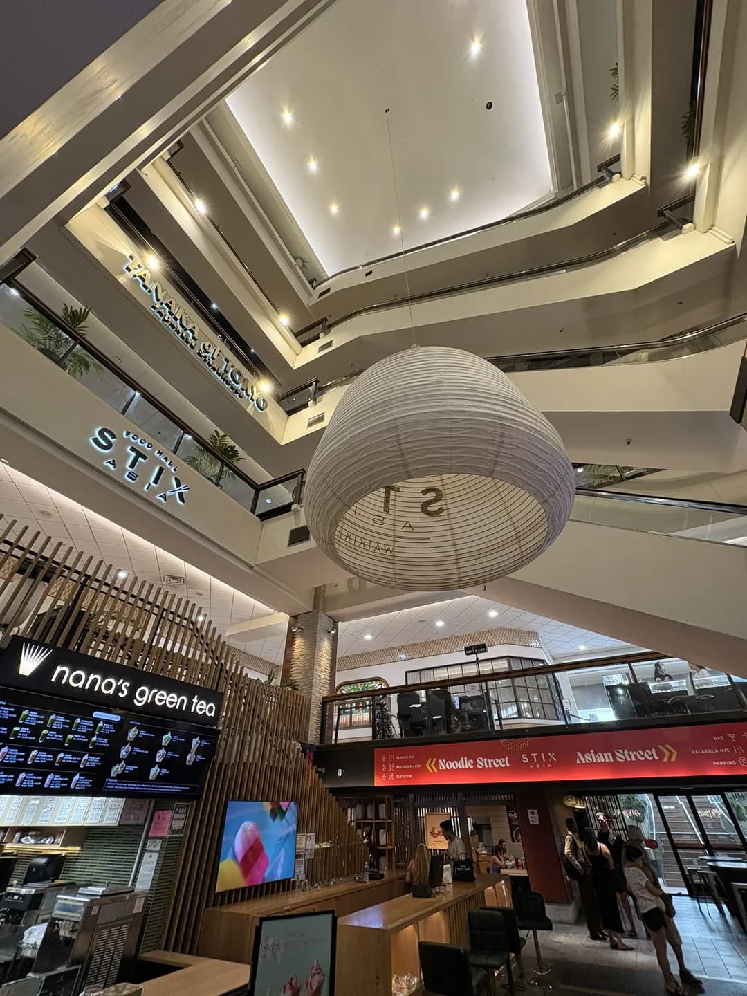 Inside the Stix Asia food hall in Waikiki, with seating and stalls near Good Chicken on the lower level