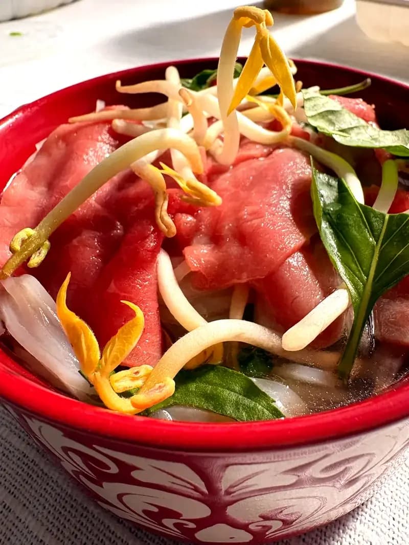 Closeup of rare steak pho in red bowl with tender beef bean sprouts and fresh basil from Ms Nguyen